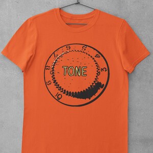 Puede incluir: Camiseta naranja con un gr&aacute;fico en blanco y negro de una perilla de guitarra con la palabra "TONE" impresa en amarillo.