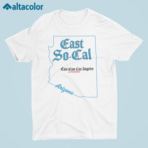 Puede incluir: Camiseta blanca con un contorno azul del estado de Arizona. El texto "East So-Cal" est&aacute; escrito en azul, en letra g&oacute;tica. Los textos "East East Los Angeles" y "PHOENIX" est&aacute;n escritos en negro, en letra m&aacute;s peque&ntilde;a.
