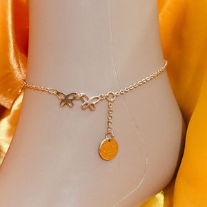 May include: A gold anklet with a delicate chain and butterfly charms. A small round charm hangs from the chain.