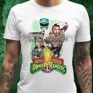 Può includere: Maglietta bianca con una grafica verde Power Rangers che presenta il Green Ranger e il logo Mighty Morphin Power Rangers. Il testo "Artwork by Hellmouth on Etsy" è incluso.