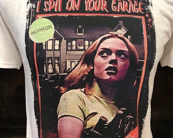 Könnte beinhalten: Weißes T-Shirt mit einem Grafikdruck eines Filmplakats für den Horrorfilm "Scream". Das Plakat zeigt eine Frau mit einem ängstlichen Ausdruck und dem Text "Tatum Riley I Spit On Your Garage".