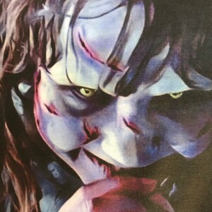 May include: A close-up of a creepy, pale-faced character with dark hair and piercing green eyes. The character has a sinister smile and appears to be wearing a dark shirt.