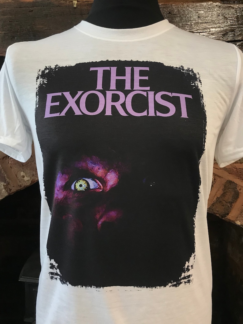 May include: White t-shirt with a black and white image of a demonic eye and the text "THE EXORCIST" in purple.