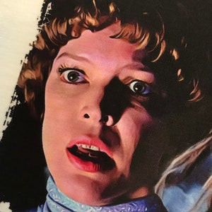 May include: A close-up of a woman's face with wide eyes and an open mouth, she is wearing a light blue collared shirt with a white pattern.