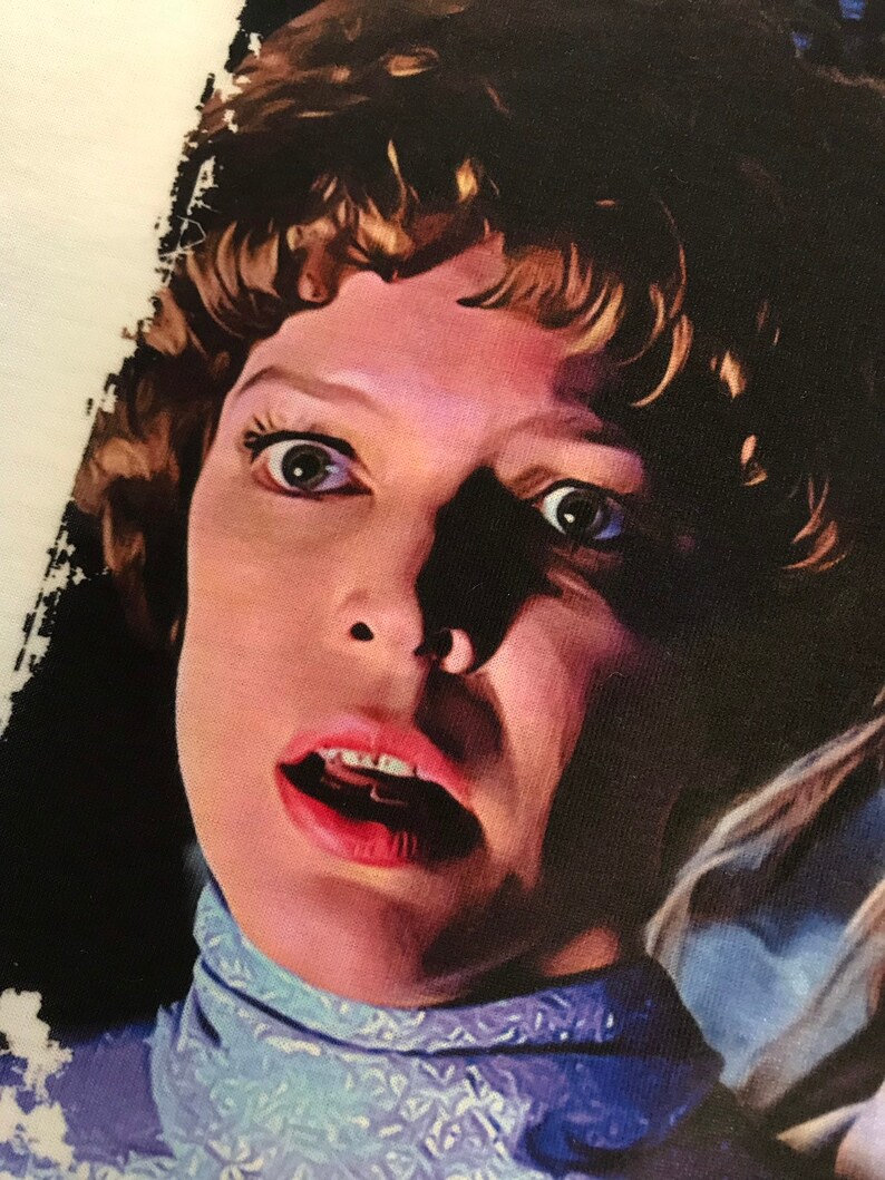 May include: A close-up of a woman's face with wide eyes and an open mouth, she is wearing a light blue collared shirt with a white pattern.
