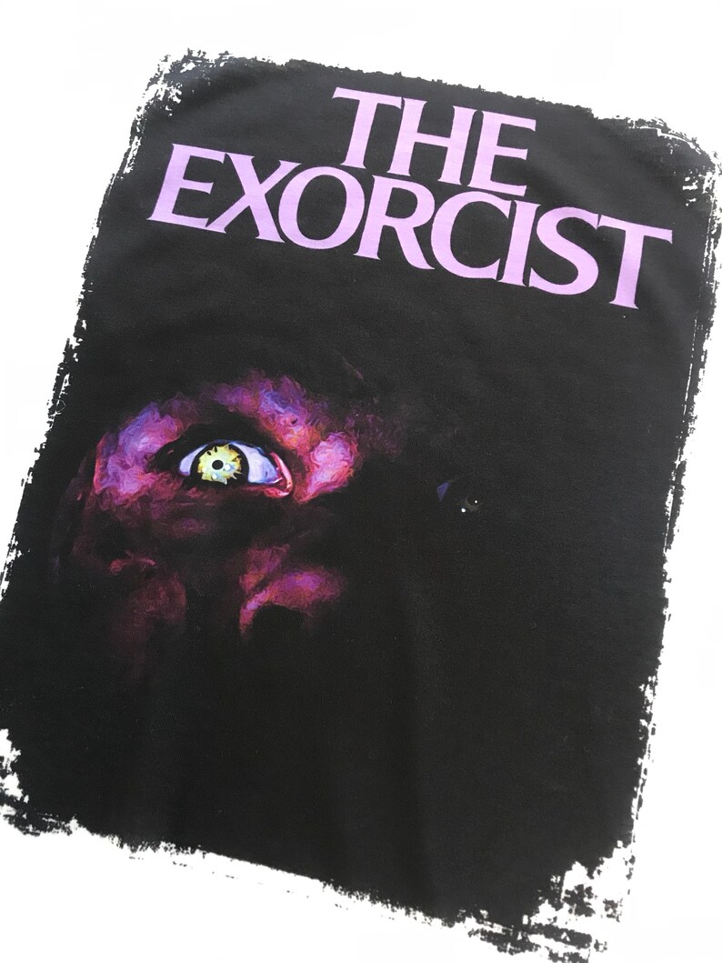 May include: A black and white graphic t-shirt with the text "THE EXORCIST" in purple lettering. The image features a close-up of a demonic eye.