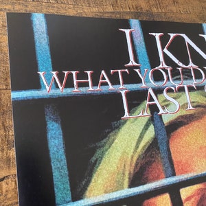 May include: A black and white poster with the text "I Know What You Did Last Summer" in white letters. The poster features a close-up of a person's face behind prison bars.
