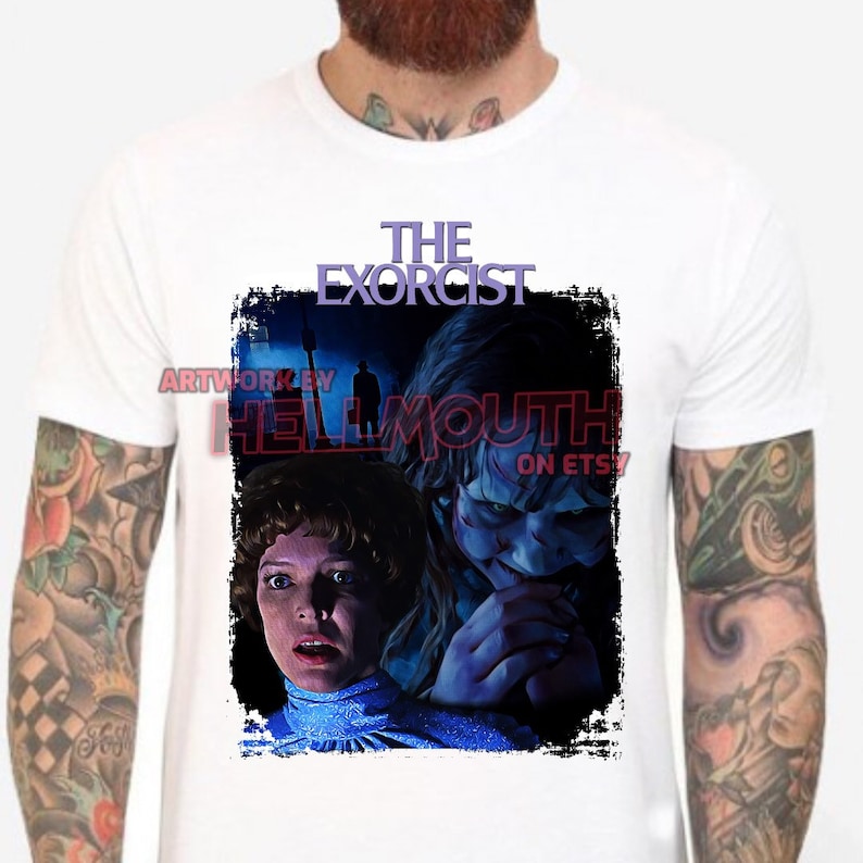 May include: A white t-shirt with a black and blue graphic of the movie "The Exorcist". The graphic features a woman with a scared expression and a demon with a menacing look. The text "THE EXORCIST" is printed in purple above the graphic.