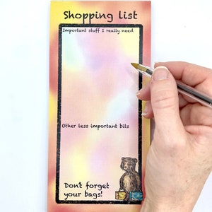 May include: A shopping list notepad with a watercolour background. The notepad has a section for "Important stuff I really need" and a section for "Other less important bits". The bottom of the notepad has a cartoon illustration of a bear with shopping bags and the text "Don't forget your bags!"