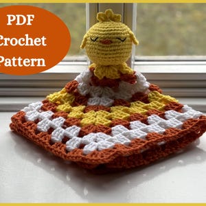 May include: A crocheted baby blanket with a yellow chick applique. The blanket is made with white, orange, and yellow yarn. The chick has black eyes and a red beak.