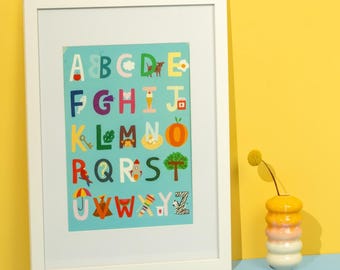 May include: A framed alphabet print with colorful letters and illustrations. The letters are set against a light blue background, and the frame is white. A decorative vase with a yellow flower is on the right.