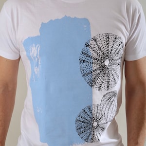 May include: White t-shirt with a blue and white abstract design featuring black and white sea urchin illustrations.