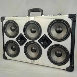 May include: A silver and black portable speaker system with six speakers and a carrying handle. The speaker system is in a suitcase-style case.