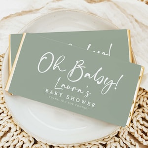 May include: Green and gold favour boxes with white text that reads "Oh Baby! Laura's Baby Shower Thank You for Coming!"