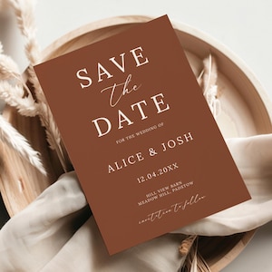 Może przedstawiać: Karta zaproszenia ślubnego w kolorze terakoty z napisem "Save the Date" w białym skrypcie i blokowych literach. Karta zawiera również imiona "Alice & Josh" oraz datę "12.04.20XX". Karta umieszczona jest na drewnianej tacy z elementami dekoracyjnymi.
