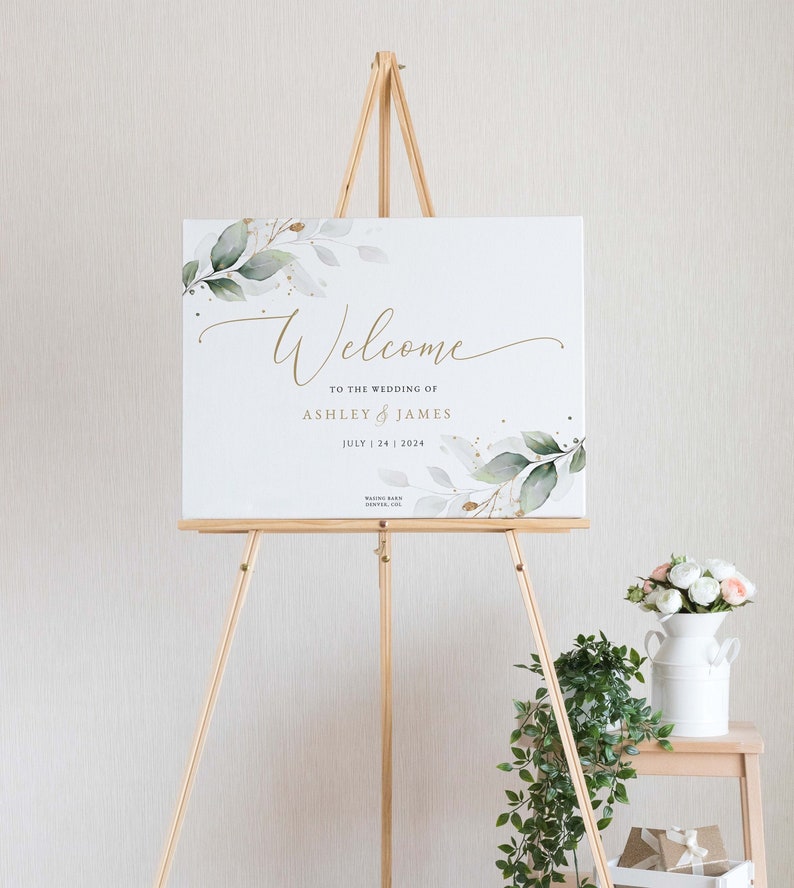 K&ouml;nnte beinhalten: Willkommensschild mit gr&uuml;nem und goldenem Laub, der Text lautet "Willkommen zur Hochzeit von Ashley & James 24. Juli 2024"