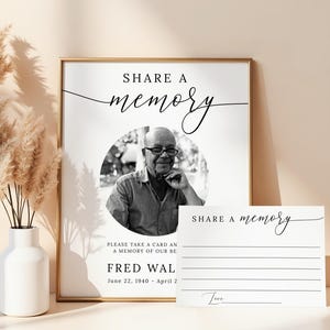 May include: A framed memorial sign with the words "Share a Memory" in elegant script. Below is a black and white photo of a man, with the text "Fred Wal" and his birth and death dates. A matching card is next to the frame.