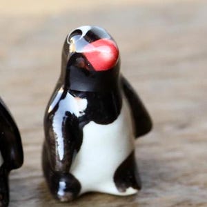 Könnte beinhalten: Eine schwarze und weiße Keramik-Pinguin-Figur mit rotem Schnabel. Der Pinguin steht auf einer Holzoberfläche.