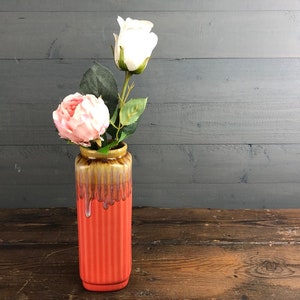 Puede incluir: Un jarrón de cerámica con un esmalte marrón y naranja, con un diseño acanalado. El jarrón está lleno de rosas artificiales rosas y blancas.