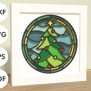 May include: A stained glass style Christmas tree design with green, blue, and yellow colors. The tree is surrounded by a circular frame with a gold border.