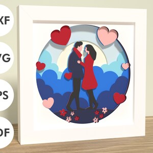 May include: A paper cut-out design of a couple standing together in front of a blue and white background with hearts and clouds. The couple is silhouetted in black and the hearts are red and pink.
