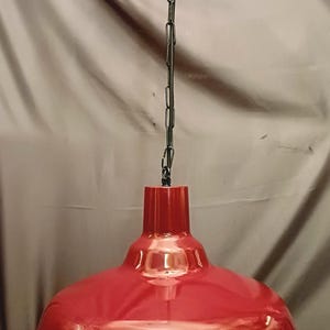 May include: A red pendant light fitting with a glossy finish. The light has a wide, bowl-shaped shade and is suspended from a black chain. The fitting is a vibrant red colour.