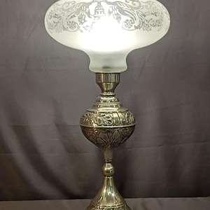 May include: An antique silver-toned table lamp with a frosted glass shade. The shade features an etched floral design and a scalloped edge. The lamp has a detailed, ornate base and a bulbous midsection, showcasing a vintage aesthetic.
