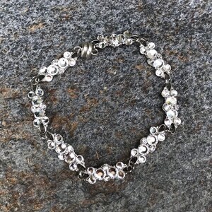 Puede incluir: Un brazalete plateado con una cadena hecha de peque&ntilde;os diamantes de imitaci&oacute;n transparentes. El brazalete tiene un cierre magn&eacute;tico.