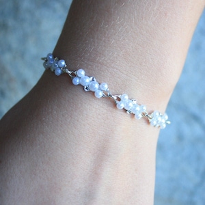 Puede incluir: Un brazalete plateado con cuentas de perlas blancas dispuestas en forma de flor.
