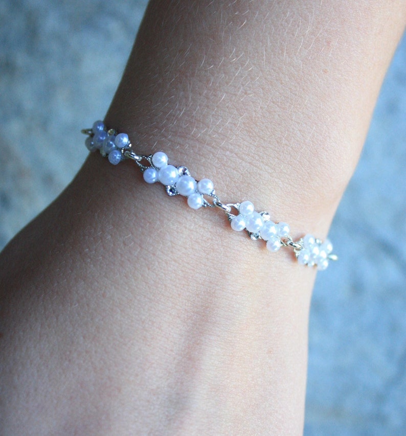 Puede incluir: Un brazalete plateado con cuentas de perlas blancas dispuestas en forma de flor.