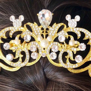 K&ouml;nnte beinhalten: Goldener Haarkamm mit einem dekorativen Design mit klaren und wei&szlig;en Strasssteinen, Perlen und Mickey-Maus-Silhouetten.