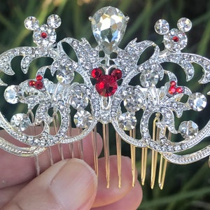 K&ouml;nnte beinhalten: Silberner Haarkamm mit einem dekorativen Design mit roten und klaren Strasssteinen. Das Design beinhaltet eine Mickey Mouse-Silhouette mit roten Ohren.