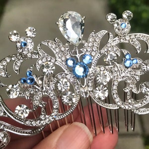 K&ouml;nnte beinhalten: Silberner Haarkamm mit floralem Design und blauen und klaren Strasssteinen. Der Kamm zeigt drei Mickey-Maus-Silhouetten.