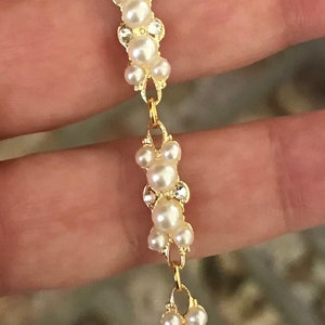 Puede incluir: Un brazalete de cadena dorada con una serie de racimos de perlas blancas. Cada racimo est&aacute; formado por cinco perlas.