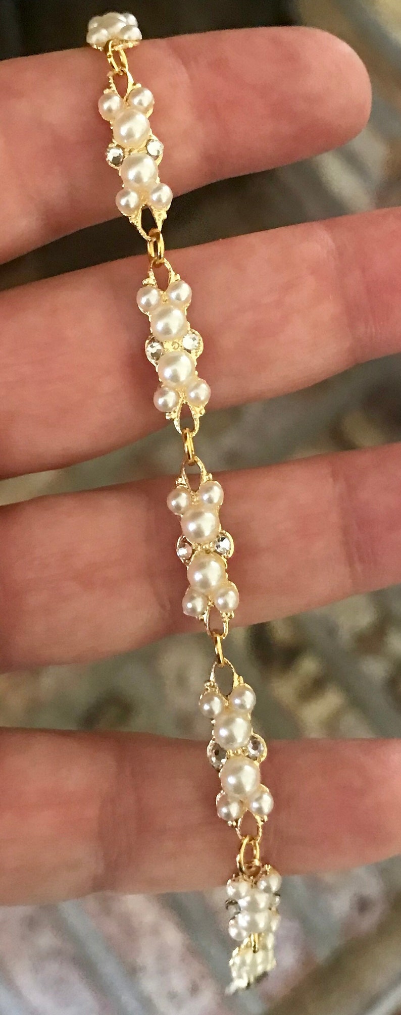 Puede incluir: Un brazalete de cadena dorada con una serie de racimos de perlas blancas. Cada racimo est&aacute; formado por cinco perlas.