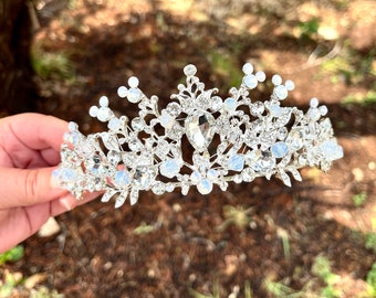 May include: A silver tiara featuring clear and iridescent rhinestones. The tiara has a delicate floral design and is ideal for a wedding or special occasion.