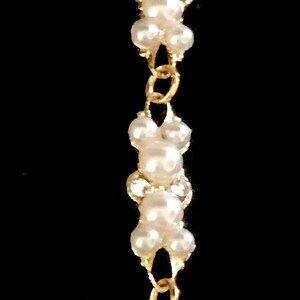 Puede incluir: Un brazalete de cadena dorada con cuentas de perlas blancas. El brazalete tiene un cierre de broche.