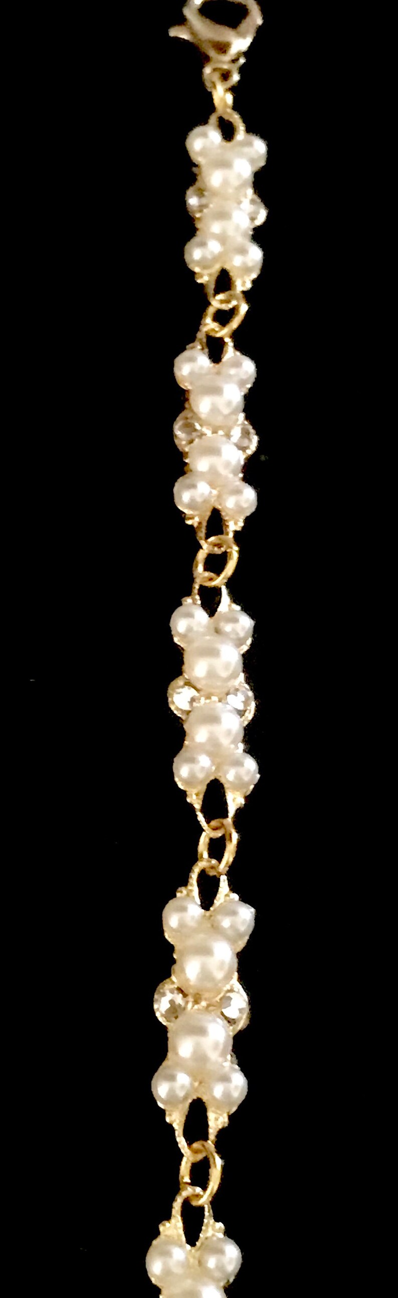 Puede incluir: Un brazalete de cadena dorada con cuentas de perlas blancas. El brazalete tiene un cierre de broche.