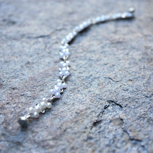 Puede incluir: Un brazalete de cadena de plata con cuentas blancas nacaradas. Las cuentas est&aacute;n dispuestas en un patr&oacute;n de peque&ntilde;as flores.