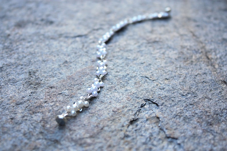 Puede incluir: Un brazalete de cadena de plata con cuentas blancas nacaradas. Las cuentas est&aacute;n dispuestas en un patr&oacute;n de peque&ntilde;as flores.