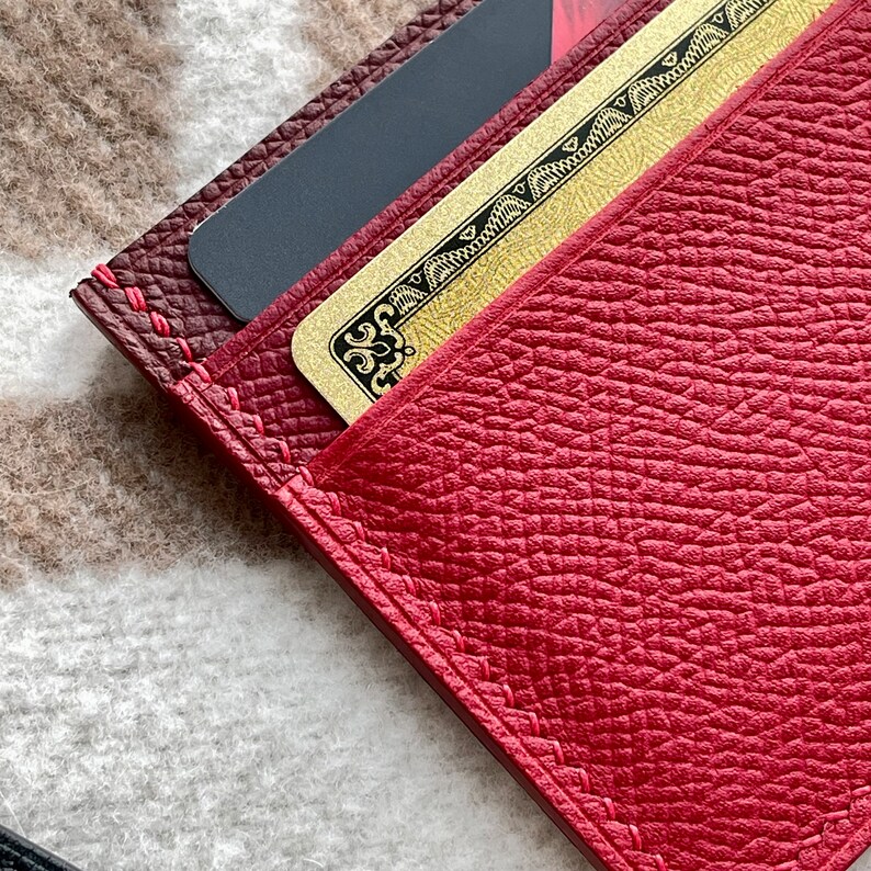 May include: A red leather wallet with a gold card inside. The wallet has a stitched edge and a textured surface.