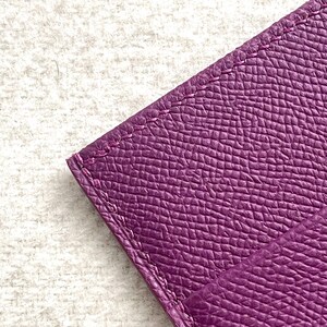 Puede incluir: Primer plano de una cartera de cuero p&uacute;rpura con una superficie texturizada y bordes cosidos.