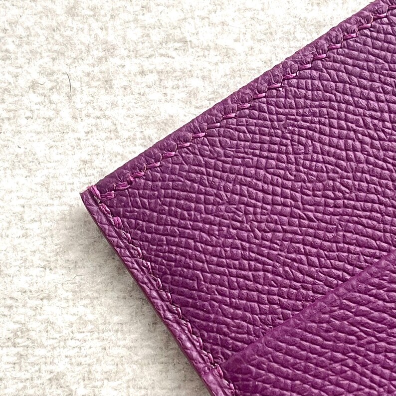 Puede incluir: Primer plano de una cartera de cuero p&uacute;rpura con una superficie texturizada y bordes cosidos.