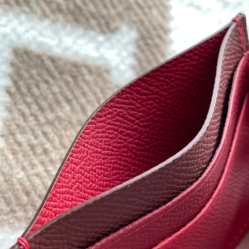 May include: A close-up of the inside of a red leather wallet with a brown leather lining. The wallet has a textured surface.