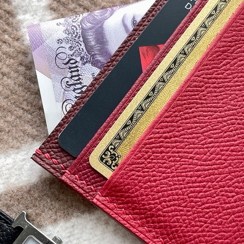 May include: A red leather wallet with a gold card inside and a black card with a red design. The wallet has a stitched edge.