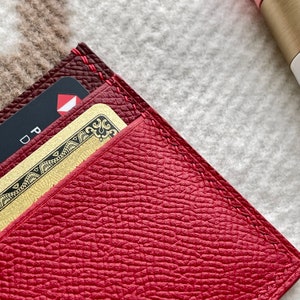 May include: Close-up of a red leather wallet with a gold credit card and a black card partially visible. The wallet has red stitching around the edges.