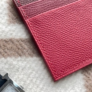 May include: Three red leather card holders with stitched edges. The card holders are arranged in a stack, with the top card holder slightly offset from the others.
