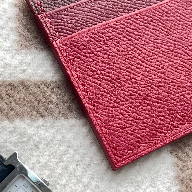 May include: Three red leather card holders with stitched edges. The card holders are arranged in a stack, with the top card holder slightly offset from the others.