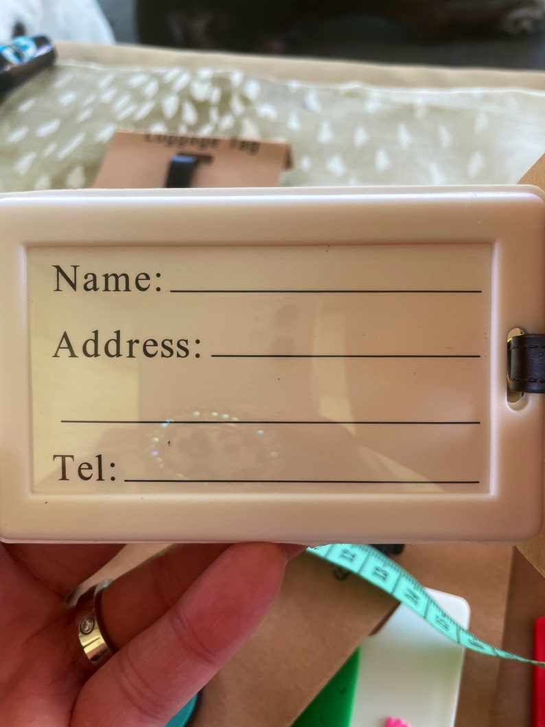 K&ouml;nnte beinhalten: Wei&szlig;er Gep&auml;ckanh&auml;nger mit schwarzem Text, der "Name:", "Adresse:" und "Tel:" lautet, mit leeren Zeilen zum Ausf&uuml;llen der Informationen.