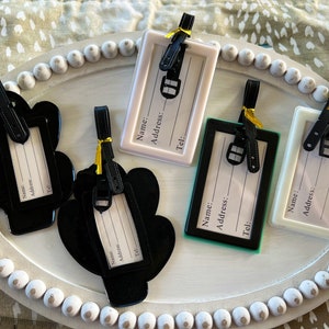 K&ouml;nnte beinhalten: F&uuml;nf Gep&auml;ckanh&auml;nger in verschiedenen Farben und Designs. Die Anh&auml;nger haben einen Platz zum Aufschreiben von Name, Adresse und Telefonnummer. Die Anh&auml;nger sind aus Kunststoff und haben ein schwarzes Band.
